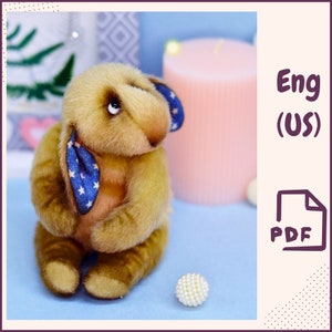 May include: A plush brown bunny with blue and white star patterned ears and a blue and white star patterned scarf. The bunny is sitting on a light blue surface with a white pearl bead next to it. The image has the text "Eng (US) PDF" in the top right corner.
