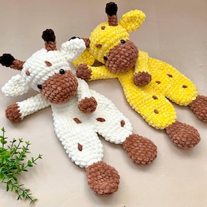 May include: Two plush giraffe toys made of soft, textured yarn. One giraffe is white with brown spots, a brown muzzle, and brown horns. The other giraffe is yellow with brown spots, a brown muzzle, and brown horns. Both have black bead eyes.