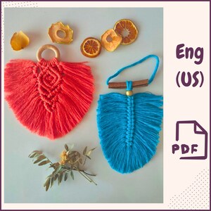 Puede incluir: Dos colgantes de pared de plumas de macramé, uno en coral y otro en azul turquesa. La pluma de coral tiene un anillo de madera en la parte superior y la pluma turquesa tiene una varilla de madera y una cuenta dorada. Ambos colgantes tienen detalles de flecos.