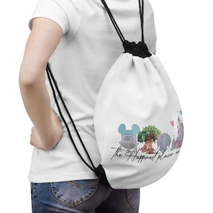May include: White drawstring backpack featuring a colorful graphic of Disney World landmarks, including the Hollywood Studios sign, a tree, and a castle. The text "The Happiest Place on Earth" is written in black script. Black drawstrings.