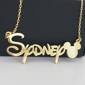 May include: Gold necklace with a nameplate pendant that says "Sydney" in a stylized font, and a Mickey Mouse head charm.