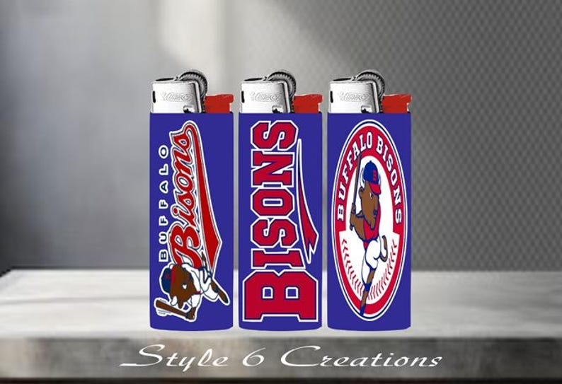 K&ouml;nnte beinhalten: Drei blaue Feuerzeuge mit roten und wei&szlig;en Grafiken des Baseballteams Buffalo Bisons. Jedes Feuerzeug hat ein anderes Design, einschlie&szlig;lich des Teamnamens und des Maskottchens. Die Feuerzeuge werden auf einer neutralen Oberfl&auml;che pr&auml;sentiert.