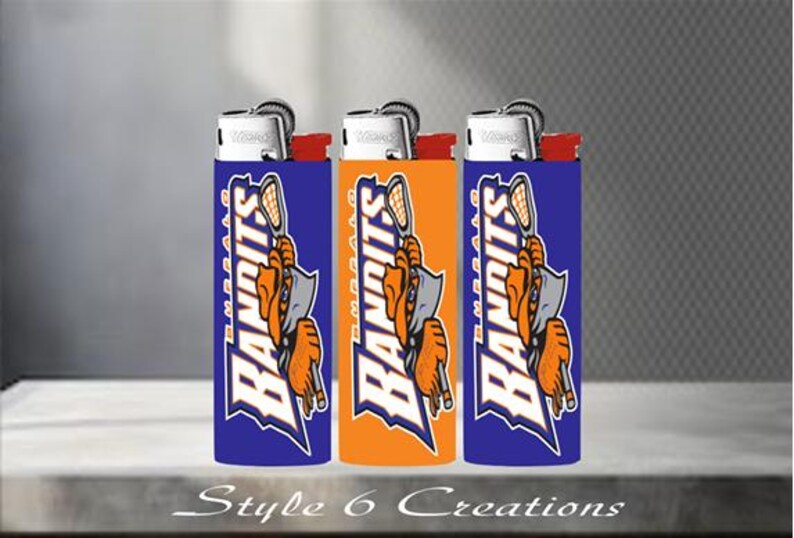 K&ouml;nnte beinhalten: Drei Feuerzeuge mit einem blau-orange-wei&szlig;en Design mit dem Wort "Bandits" und einer Lacrosse-Spieler-Grafik. Die Feuerzeuge haben einen silbernen Deckel und rote Akzente. Der Text "Style 6 Creations" befindet sich unten.