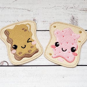 Peut inclure: Deux écussons brodés en forme de tranches de pain grillé. L'un représente du beurre de cacahuète, l'autre de la gelée. Les deux ont des visages souriants avec des yeux noirs et des joues roses. Les tranches de pain sont beiges avec une bordure beige.