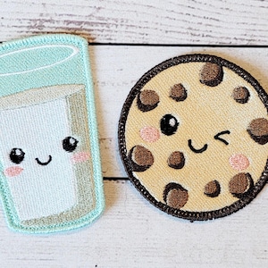 Pode incluir: Dois patches bordados para passar a ferro, um de um copo de leite com uma cara fofa e o outro de um biscoito de chocolate com uma cara a piscar o olho.