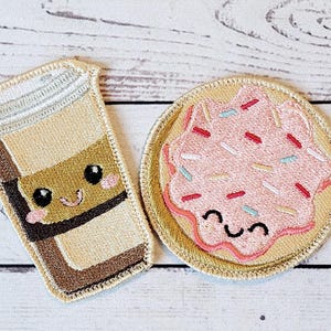Può includere: Due toppe ricamate, una con una tazza di caffè e l'altra con una ciambella. Entrambe le toppe hanno facce sorridenti.