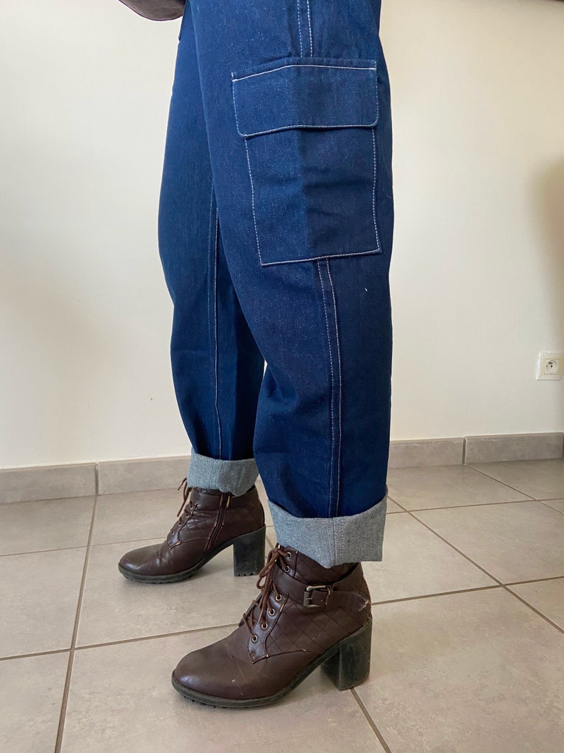 Op de afbeelding: Donkerblauwe denim cargo broek met een grote cargotas op het rechterbeen. De broek is omgeslagen aan de onderkant en de persoon draagt ​​bruine enkellaarsjes.