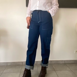 Op de afbeelding: Een vrouw draagt een wit overhemd met knopen, een donkerblauwe jeans met witte stiksels en bruine enkellaarsjes. De jeans heeft grote zakken aan de zijkanten.