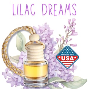 May include: Lilac Dreams car air freshener with a wooden diffuser and a clear glass bottle filled with yellow liquid. The air freshener is hanging from a rope with a knot. The image is surrounded by purple lilac flowers and green leaves. The text "Made in the USA" is on a red, white, and blue star-shaped label.