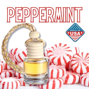 May include: A clear glass bottle with a yellow liquid inside, a wooden stopper, and a gold rope hanging from it. The bottle is surrounded by red and white peppermint candies. The bottle has a label that says "Peppermint" and a sticker that says "Made in the USA".