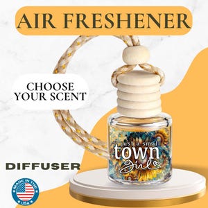 May include: Air freshener with a wooden top and a glass bottle featuring a sunflower design. The text "just a small town Girl" is visible on the bottle. The product is displayed on a white platform with the text "Choose Your Scent" and "Diffuser".