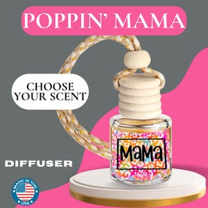 May include: An air freshener diffuser with the text "Poppin' Mama" and "Choose Your Scent." The glass bottle has a colorful design with the word "Mama" in a black frame. The product is on a white stand with a gold rim.