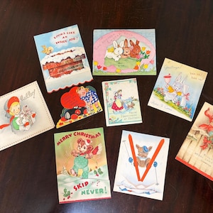 May include: A collection of vintage greeting cards featuring various illustrations. The cards depict themes such as Easter, Christmas, and general well wishes. The cards have colorful illustrations of bunnies, children, and other festive imagery.