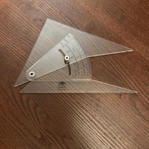 May include: A clear plastic drafting tool with a protractor and adjustable arms. The tool has degree markings and a pivot point for angle adjustments. The tool is designed for measuring and drawing angles.