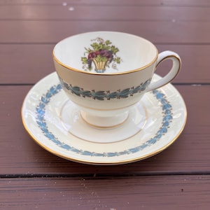 May include: A white teacup and saucer with a gold rim and a blue and gold floral design. The teacup has a handle and the saucer has a scalloped edge.