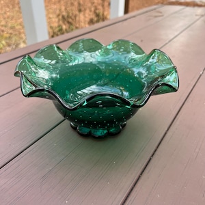 May include: A green glass bowl with a ruffled edge and a textured surface. The bowl has a small base and is perfect for serving snacks or desserts.