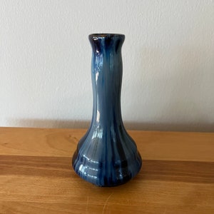 May include: A small blue and black ceramic vase with a narrow neck and a wide base. The vase has a striped pattern.