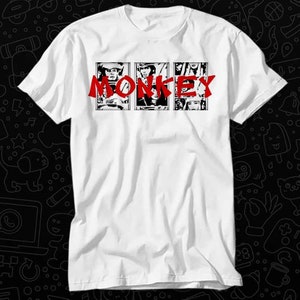 May include: White t-shirt with a black and white graphic of four people in a row with the word "MONKEY" in red letters above them.