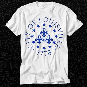 May include: White t-shirt with a blue circle graphic that says "City of Louisville 1778" with three blue fleur-de-lis and stars around the circle.