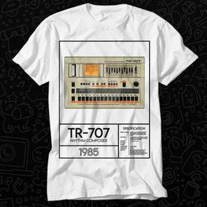 May include: A white t-shirt with a graphic of a Roland TR-707 Rhythm Composer. The graphic includes the text "TR-707 Rhythm Composer 1985" and a specification list.