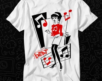 Puede incluir: Camiseta blanca con una ilustración en blanco y negro de una mujer con una camisa roja y una falda negra. La mujer sostiene un micrófono y está de pie sobre una nota musical. El texto "The English Beat" está impreso en la camiseta.