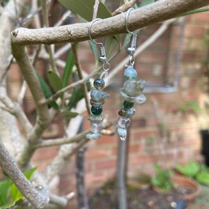 May include: A pair of silver dangle earrings with green and clear gemstone beads. The earrings are hanging from a branch.