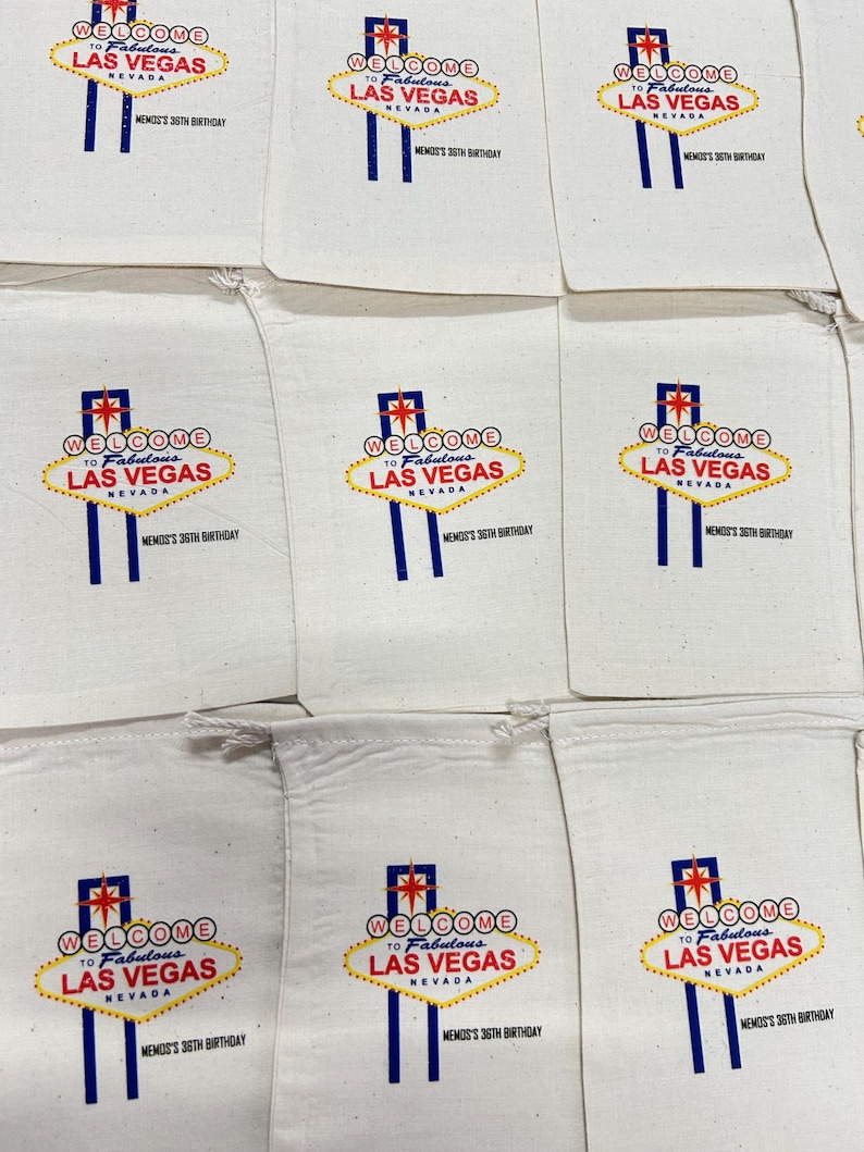 Puede incluir: Bolsas de tela blancas con un dise&ntilde;o impreso del ic&oacute;nico letrero "Welcome to Fabulous Las Vegas" en rojo, amarillo y azul. El texto "MEMOS'S 36TH BIRTHDAY" est&aacute; impreso debajo. Las bolsas est&aacute;n dispuestas en una cuadr&iacute;cula.