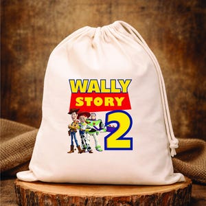 Puede incluir: Una bolsa blanca con cord&oacute;n, con el texto "WALLY STORY 2" en amarillo y rojo, con los personajes de dibujos animados Woody, Jessie y Buzz Lightyear. La bolsa est&aacute; sobre una superficie de madera.