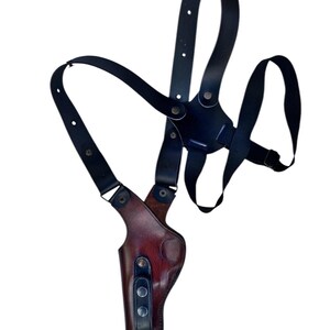 Puede incluir: Una funda de hombro de cuero negro con un bolsillo para pistola de cuero marr&oacute;n. La funda tiene correas ajustables y herrajes met&aacute;licos. El dise&ntilde;o es para porte oculto.