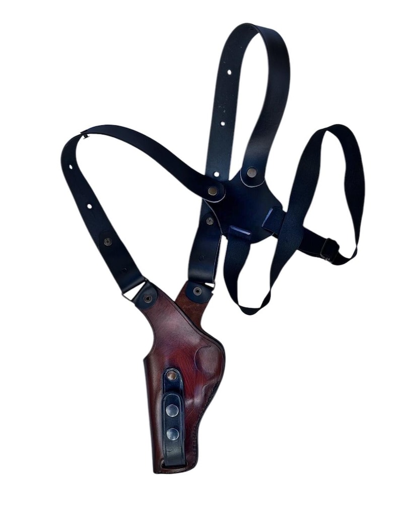 Puede incluir: Una funda de hombro de cuero negro con un bolsillo para pistola de cuero marr&oacute;n. La funda tiene correas ajustables y herrajes met&aacute;licos. El dise&ntilde;o es para porte oculto.
