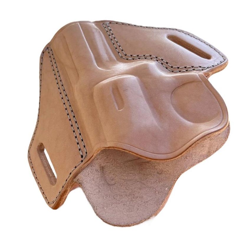 May include: A light brown leather holster with black stitching. The holster has a molded design to fit a handgun, with a loop and a cutout for a belt. The interior is a lighter shade of brown.