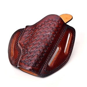 Op de afbeelding: Een bruine leren holster met een geweven patroon. De holster heeft een klep die de opening bedekt en een riemlus.