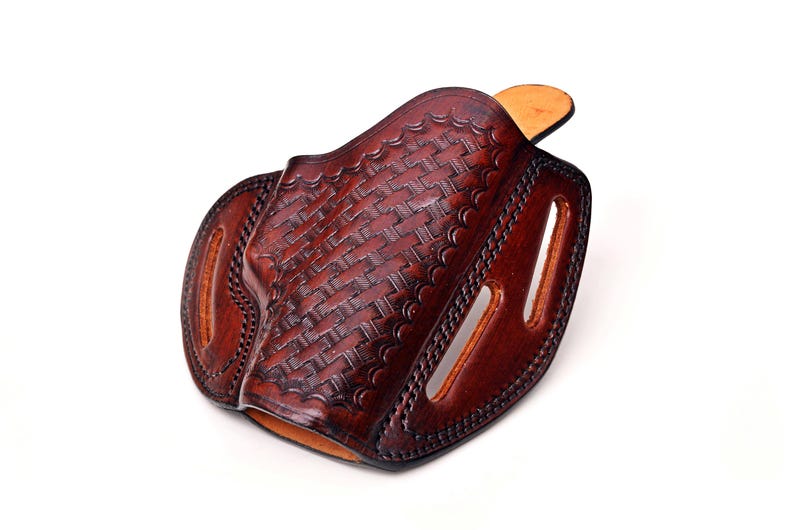 Op de afbeelding: Een bruine leren holster met een geweven patroon. De holster heeft een klep die de opening bedekt en een riemlus.