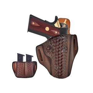 Puede incluir: Una funda de cuero marrón con un patrón tejido, que sostiene una pistola negra con empuñadura de vetas de madera. Dos cargadores negros están en un portacargadores de cuero a juego. Sobre fondo blanco.