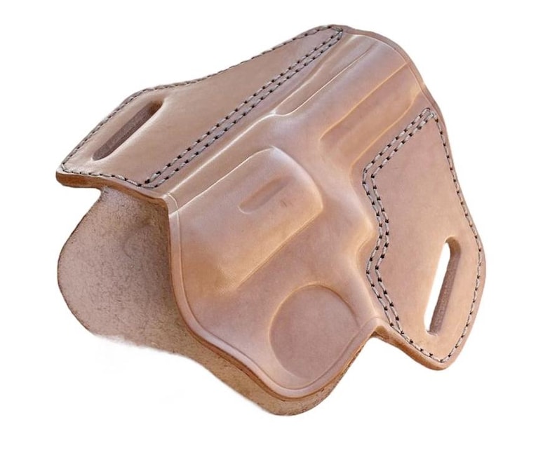 May include: A light brown leather holster with a molded design to fit a revolver. The holster has black stitching around the edges and features belt loops. The interior is a lighter shade of brown.