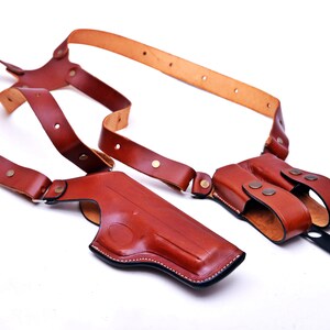 May include: A brown leather shoulder holster with two separate compartments for carrying a firearm and extra ammunition. The holster has adjustable straps and a secure closure.