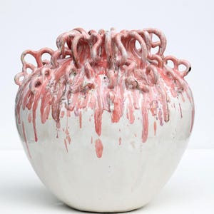 Könnte beinhalten: Eine Keramikvase mit bauchigem Körper und schmaler Öffnung. Die Basis ist mit einer glatten, glänzenden weißen Glasur versehen. Der obere Teil zeigt eine dichte Ansammlung von rosa, schleifenartigen Keramik-Extrusionen mit tropfendem Glasureffekt.