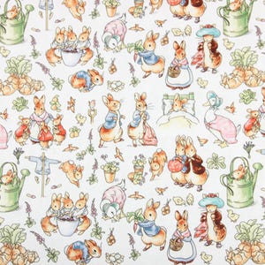 Op de afbeelding: Witte stof met een herhaald patroon van illustraties met Peter Rabbit en zijn vrienden. Het ontwerp omvat konijnen in blauwe jasjes en roze jurken, samen met gieters en groenten, waardoor een charmante scène ontstaat.