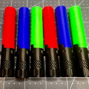May include: Six colorful, cylindrical objects with black bases are arranged in a row. The cylinders are red, blue, and green. The black bases have a textured pattern. The objects appear to be 3D printed.