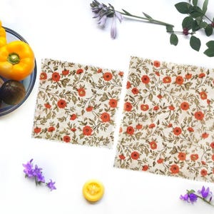 May include: Two floral patterned beeswax food wraps, one larger and one smaller, on a white surface. The wraps are made of fabric and are designed to be reusable and sustainable.