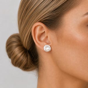 May include: A single white baroque pearl stud earring with an irregular, organic, and rounded shape. The pearl features a lustrous, iridescent surface with subtle ridges and a smooth, polished finish, secured by a simple metal post backing.
