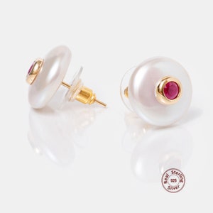 May include: A pair of pearl earrings with a small red gemstone set in gold. The earrings are made of sterling silver.
