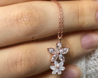 May include: A delicate rose gold necklace with a two-tiered flower pendant. The top flower is made of clear cubic zirconia stones, while the bottom flower is made of white mother-of-pearl.