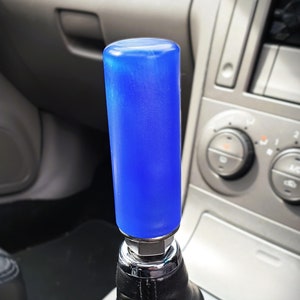 Może przedstawiać: Gałka zmiany biegów do samochodu w kolorze niebieskim i srebrnym z czarną skórzaną osłoną.