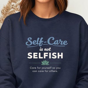 May include: Navy blue sweatshirt with the text "Self-Care is not SELFISH" in white and light blue. Below the text is a lotus flower graphic and the words "Care for yourself so you can care for others."
