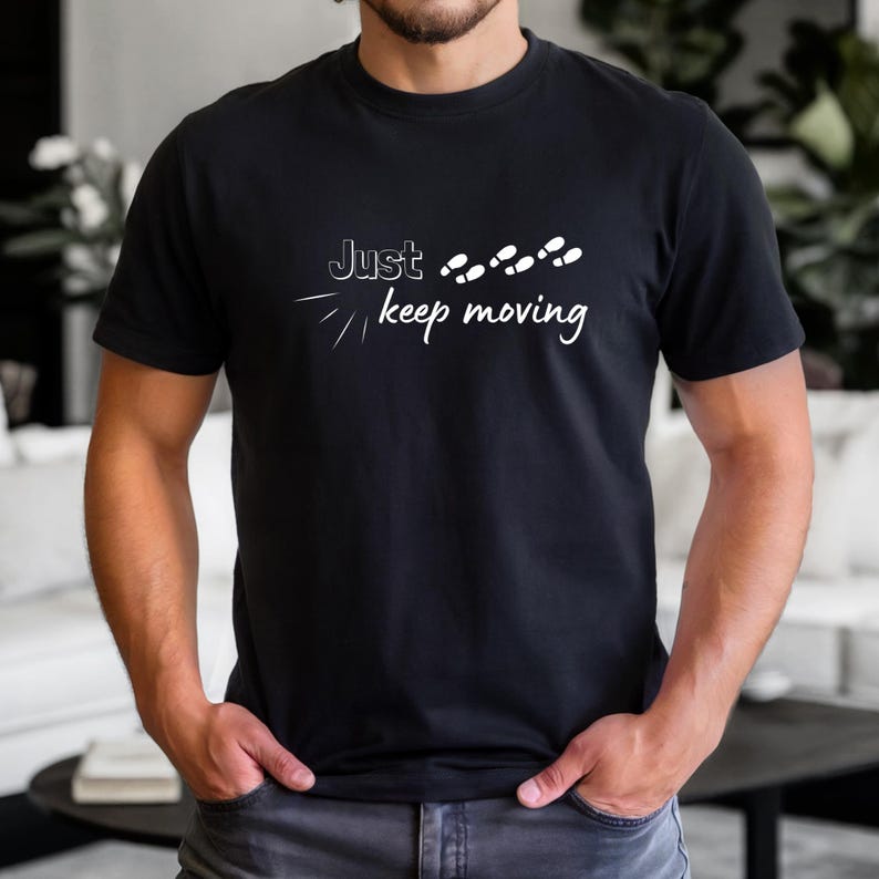 Peut inclure: T-shirt noir avec l'inscription blanche "Just keep moving" et un motif de pas. Le t-shirt &agrave; manches courtes semble &ecirc;tre en coton. Le design est centr&eacute; sur la poitrine.