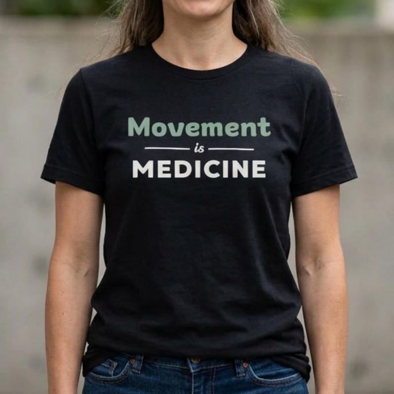 May include: Black t-shirt with the text "Movement is Medicine" in white and green lettering. The shirt is a crew neck style and appears to be made of a soft material. The text is centered on the front of the shirt.