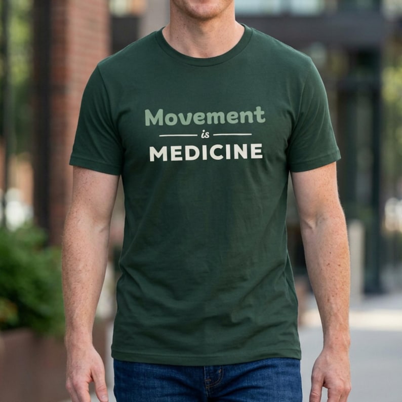 May include: Dark green t-shirt with the text "Movement is Medicine" in a light grey font. The text is centered on the chest. The shirt has short sleeves and a crew neck.