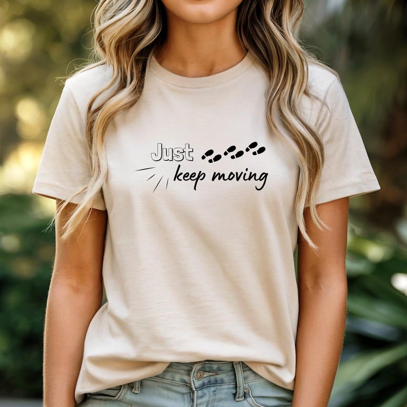 Peut inclure: T-shirt beige avec l'inscription noire &laquo;&nbsp;Just keep moving&nbsp;&raquo; et des empreintes de pas noires. Le t-shirt a un col rond et des manches courtes. Le design est simple et motivant.