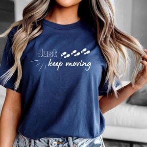 Peut inclure: T-shirt bleu marine avec l'inscription blanche "Just keep moving". Le motif comprend des empreintes de pas blanches. Le t-shirt est &agrave; col rond et &agrave; manches courtes.